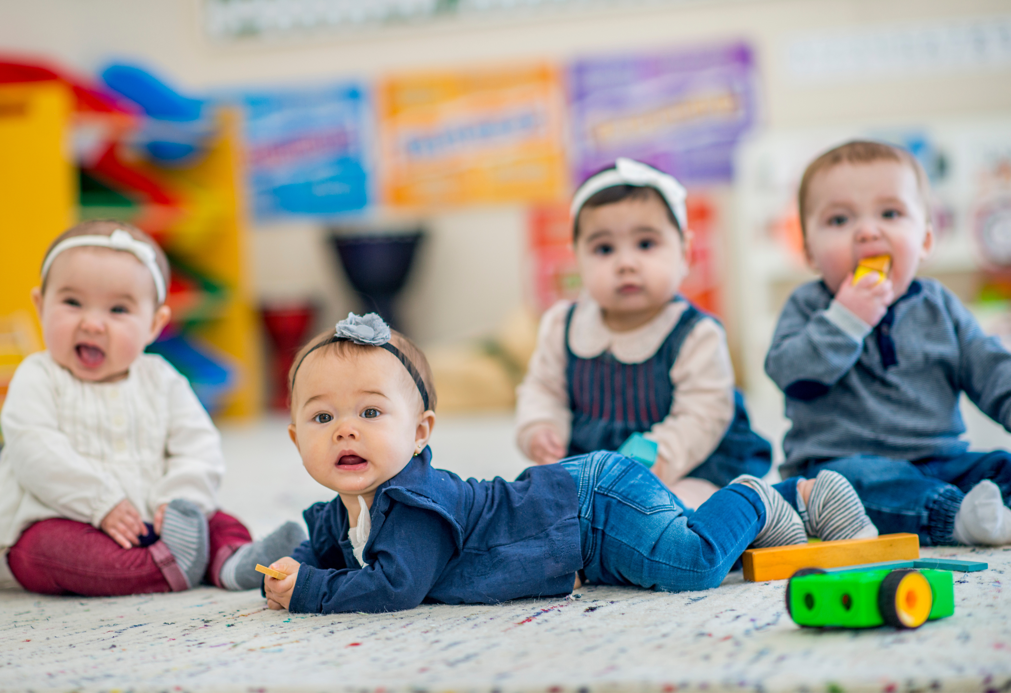 Photo of four babies on the floor attentively looking at something out of view