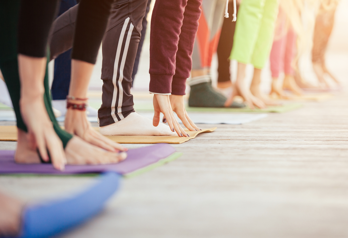 Photo of the feet of a row of people on workout mats who are stretching down to touch the floor