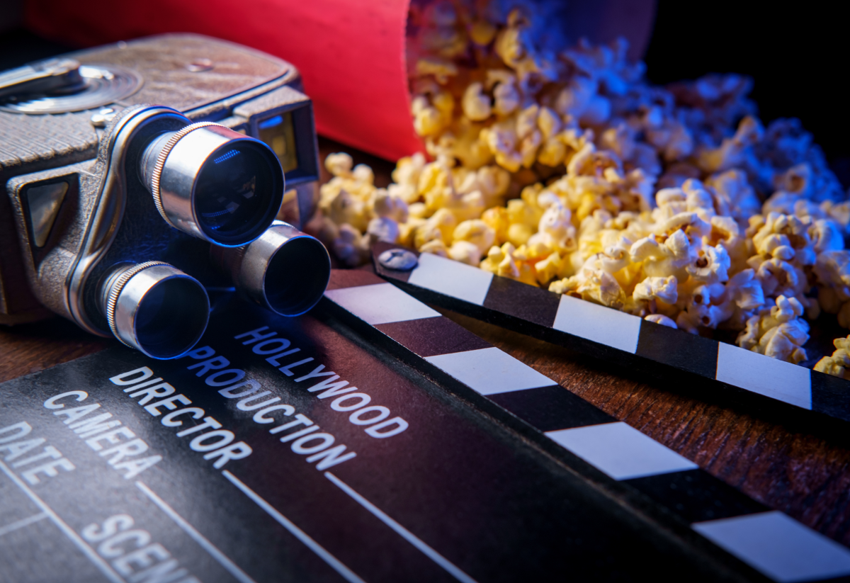 Photo of a movie projection camera on a table beside a clapperboard and spilled popcorn